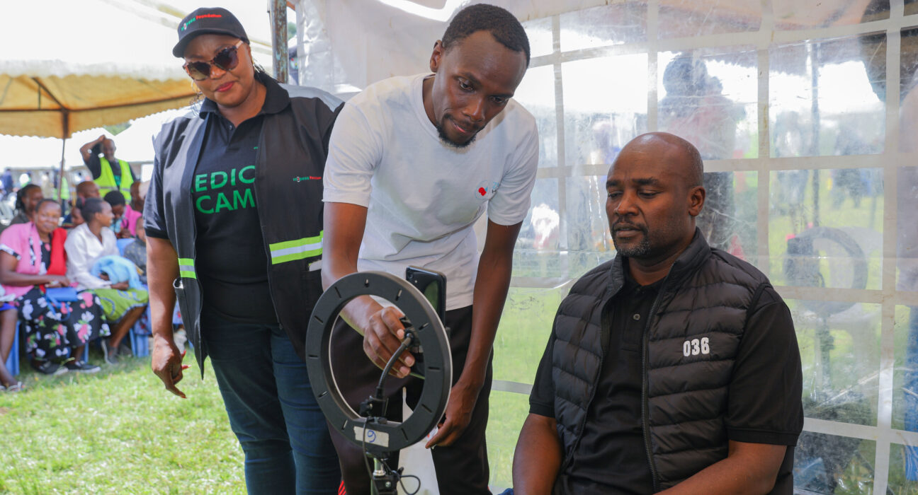 Safaricom and M-Pesa Foundations Programmes Manager Sophie Onyango (left) looks on as Bomet County Governor H.E Dr. Hillary Barchok (seated) gets an AI screening during an M-Pesa foundation medical camp.