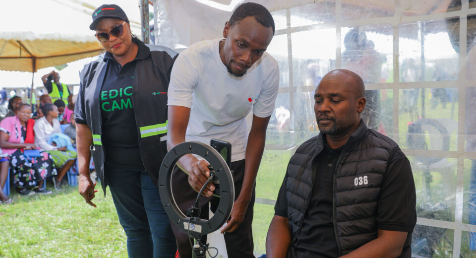 Safaricom and M-Pesa Foundations Programmes Manager Sophie Onyango (left) looks on as Bomet County Governor H.E Dr. Hillary Barchok (seated) gets an AI screening during an M-Pesa foundation medical camp.